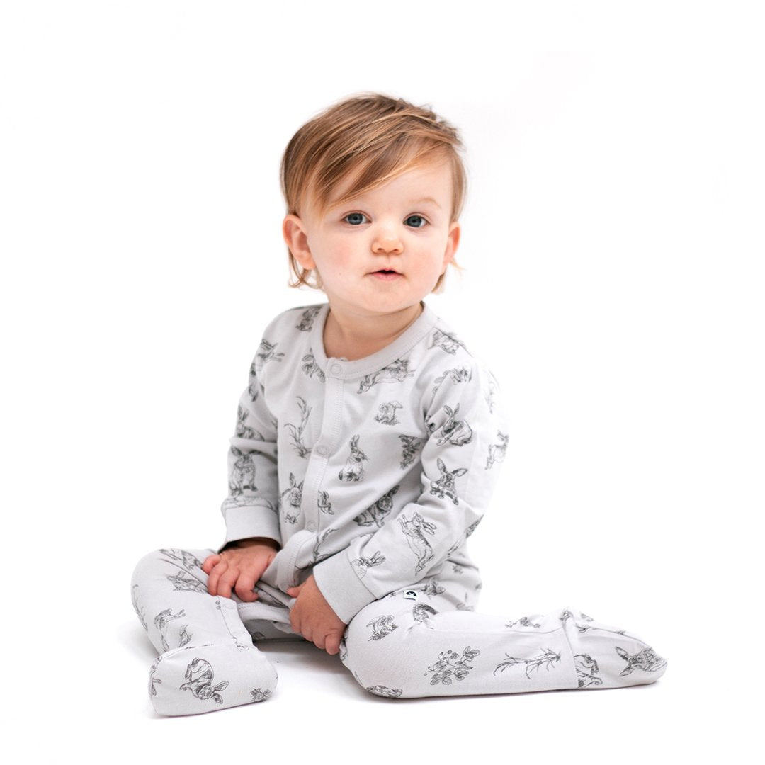 Toddler wearing organic cotton sleepsuits in grey with rabbit design and long sleeves. Snap buttons down the front.